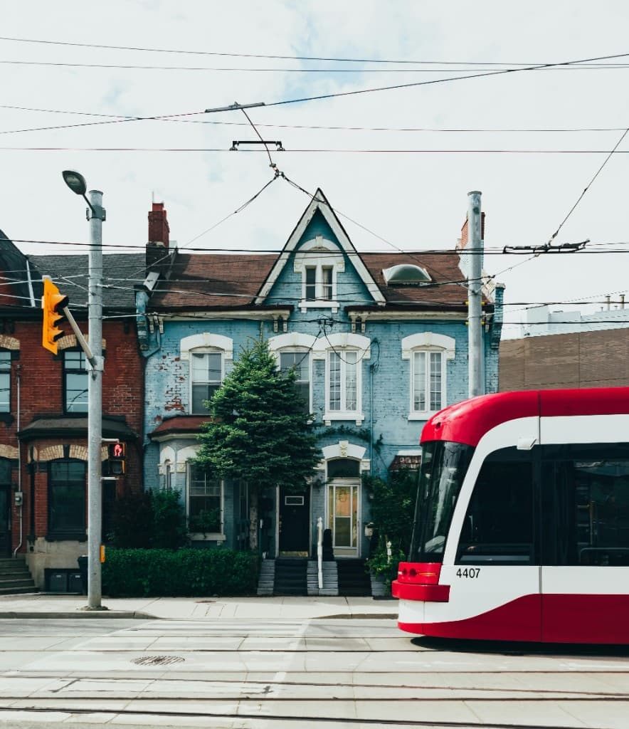 Urban street with streetcar tracks, a Victorian brick house, and a Toronto streetcar