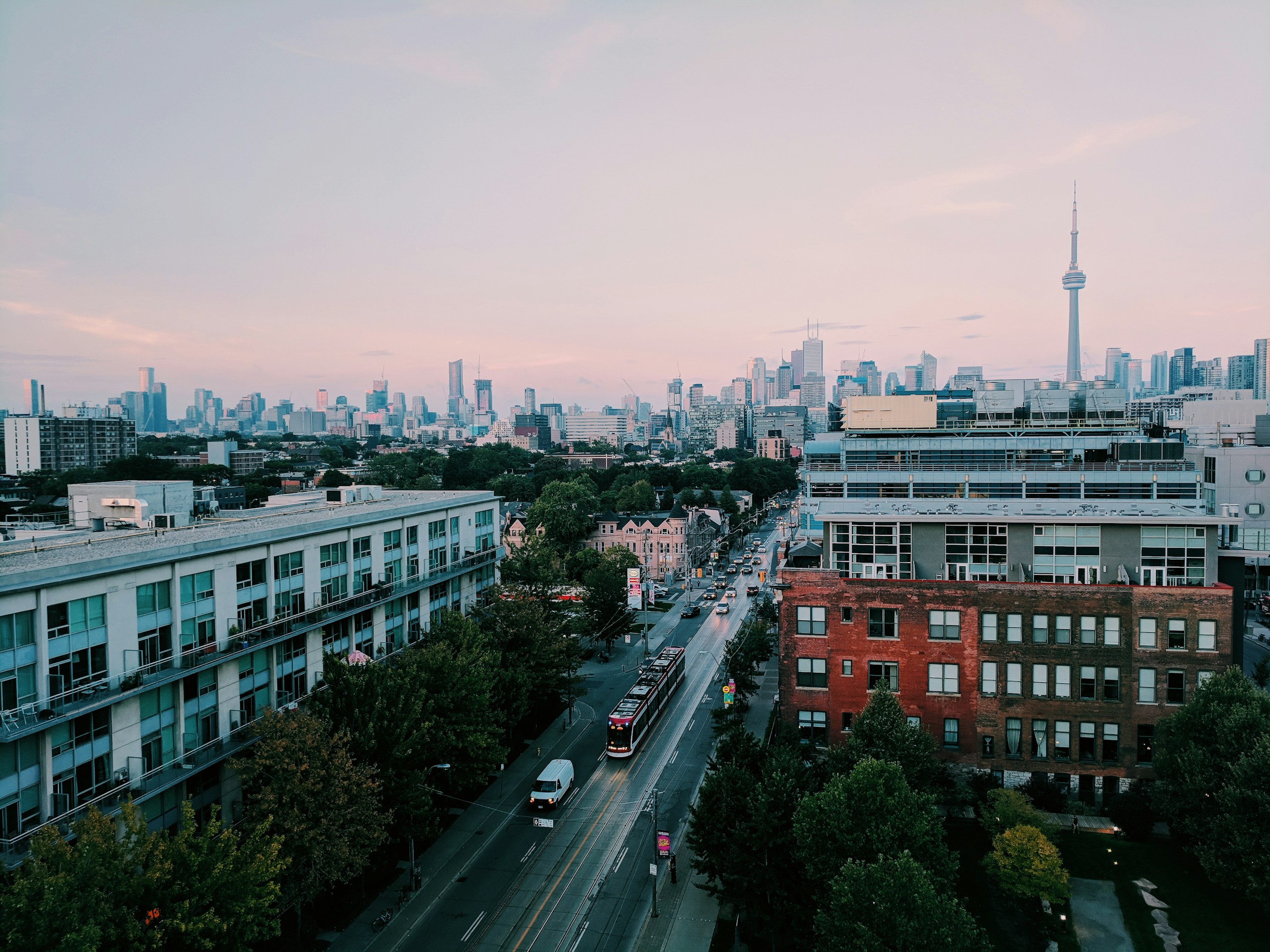 Toronto streetscape at dusk with streetcar, Victorian brick buildings, and the CN Tower skyline