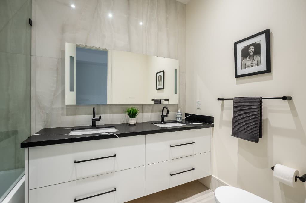 Spotless bathroom with double white vanity, black marble countertop, matte black fixtures, and large mirror in an HSG-managed Toronto rental