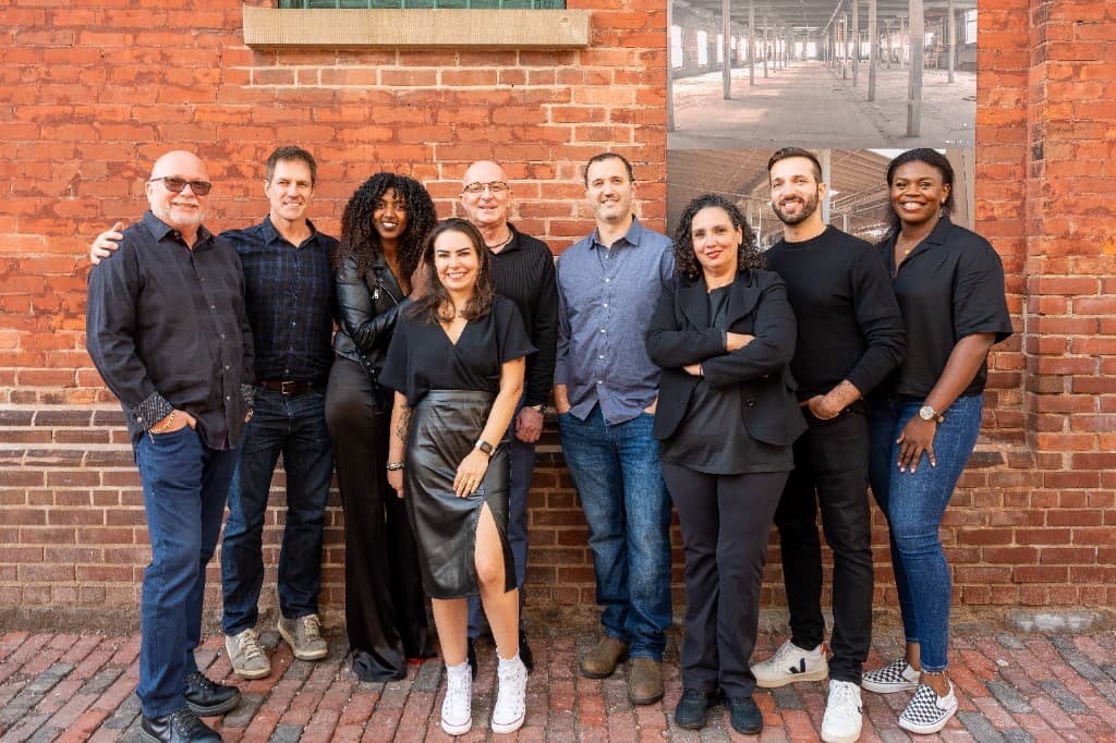Nine Host Services Group team members standing together outdoors on a cobblestone lane in front of a red brick wall